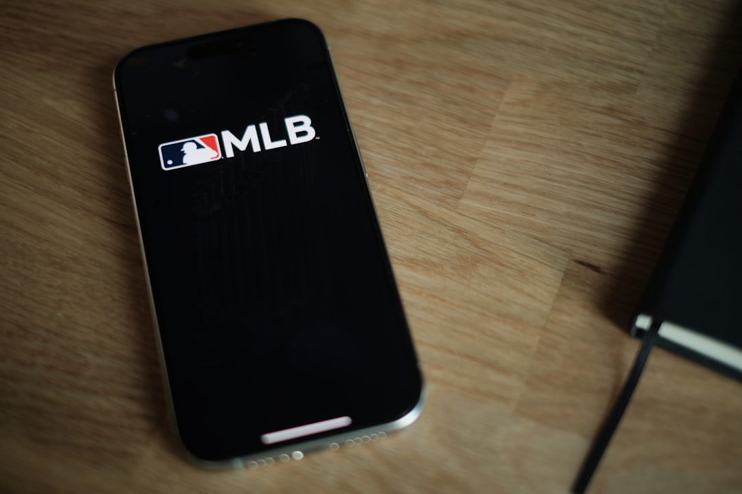 A black cell phone sitting on top of a wooden table mlb app, baseball fan, mobile phone