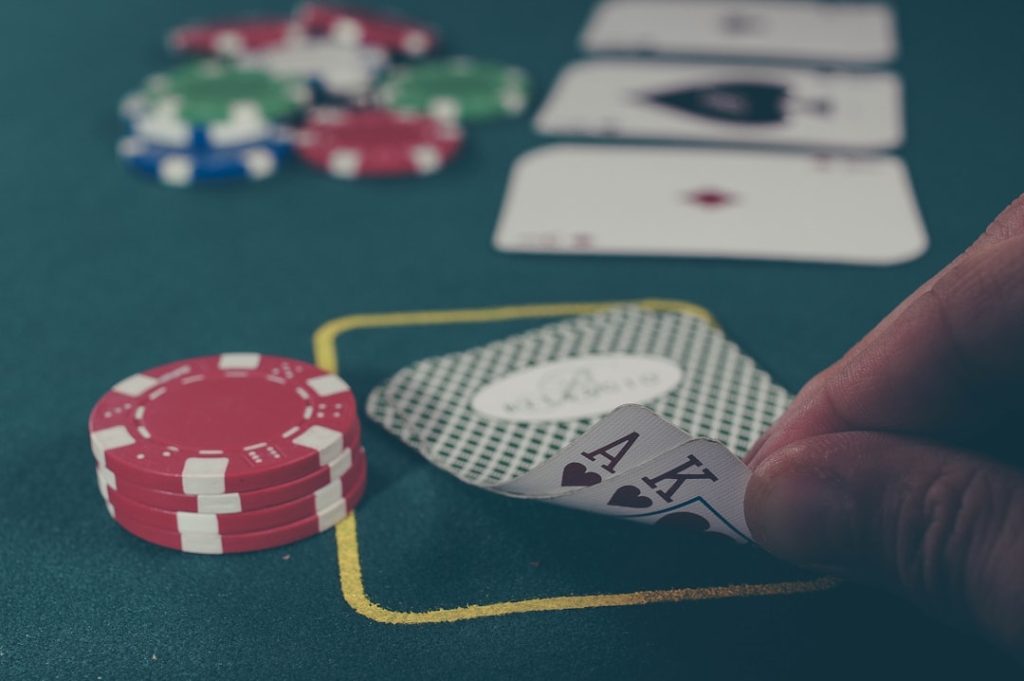 person holding black ace and king spades playing cards on poker table casino bonuses, promotions, slot spins