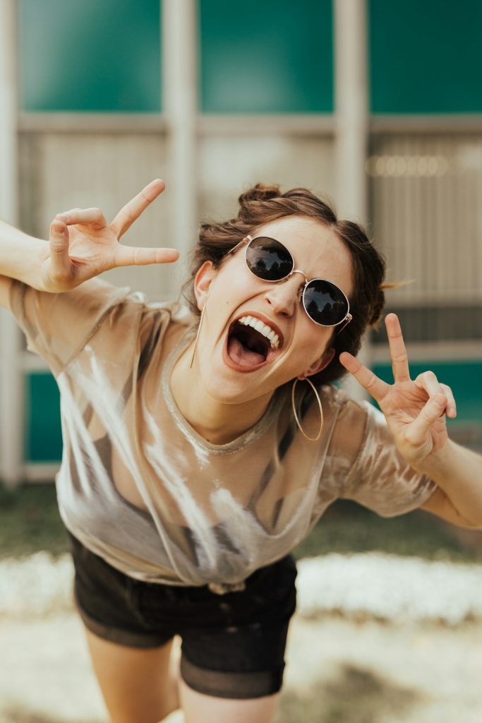selective focus photography of jolly woman using peace hand gesture happy fans, watching sports, mobile phone