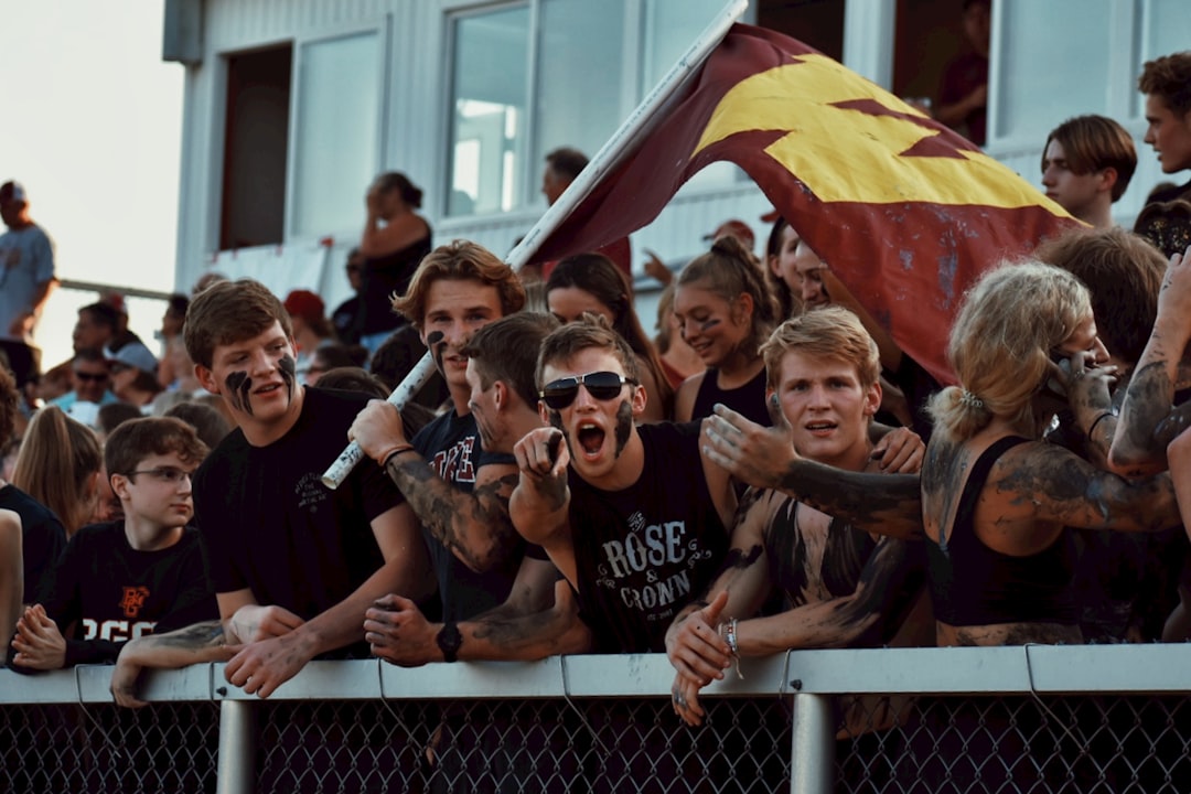 group of people holding flags during daytime grinnell college fans cheering football game
