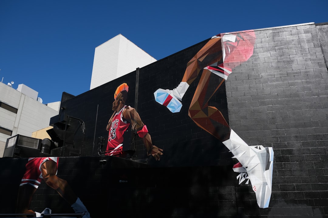 man in black jacket and pants sitting on black concrete wall during daytime post malone style,fashion courtside,nba culture,mural tribute
