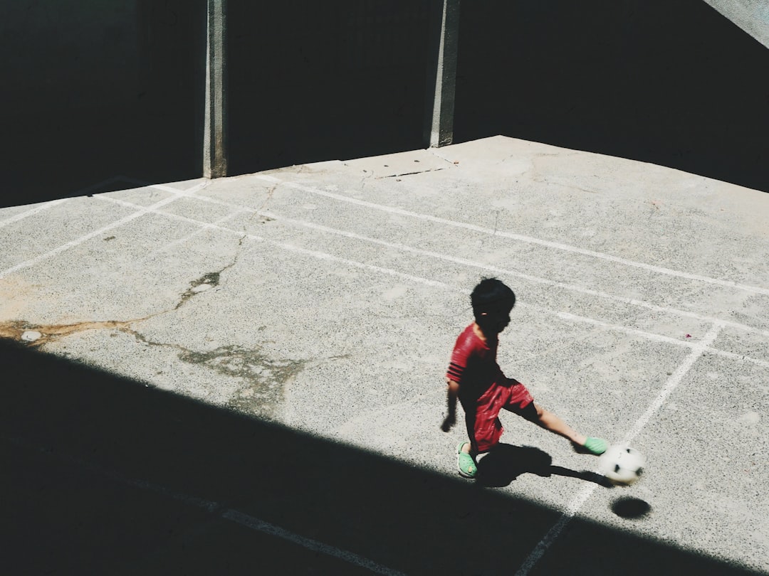 boy in red and white long sleeve shirt playing soccer during daytime two footed shooting, football skills, ronaldo goal
