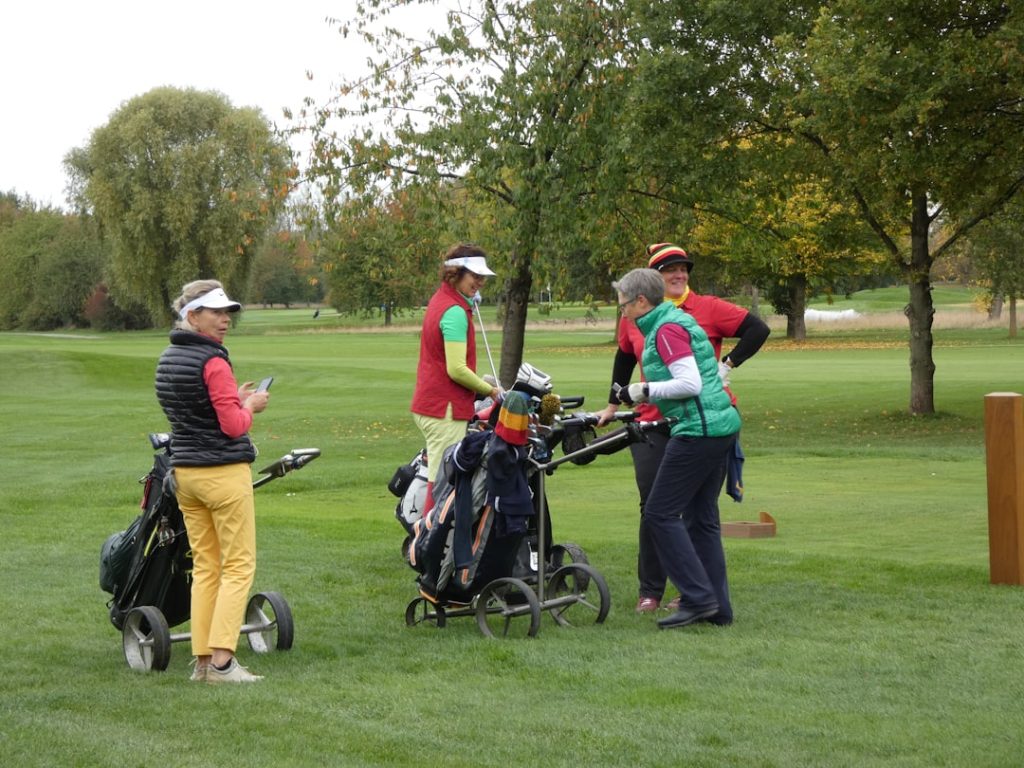 Four women gathered around golf bags on a course golfer putting, tournament leaderboard, golf crowd