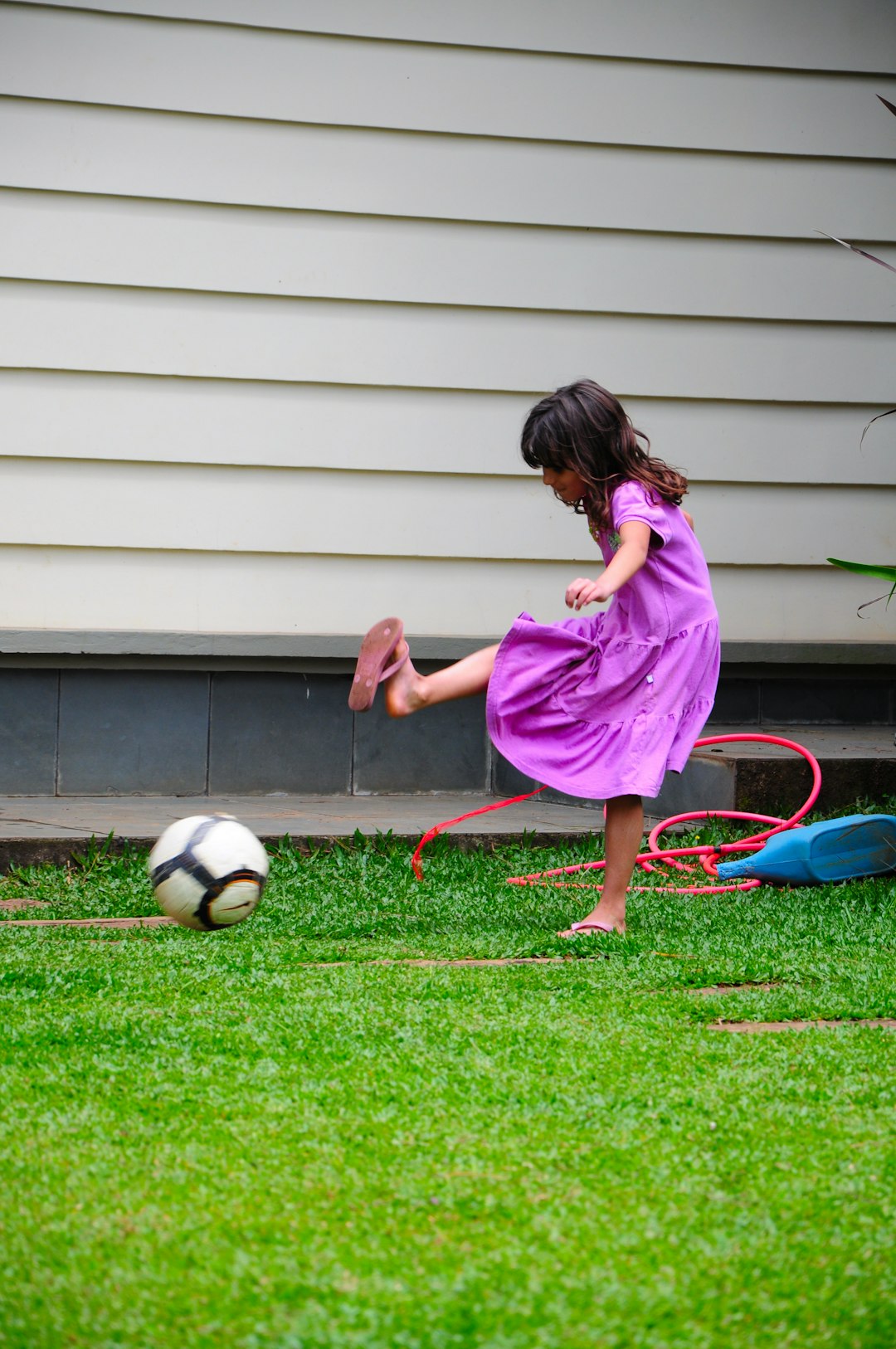 girl in pink dress playing soccer dribbling, soccer cones, backyard practice