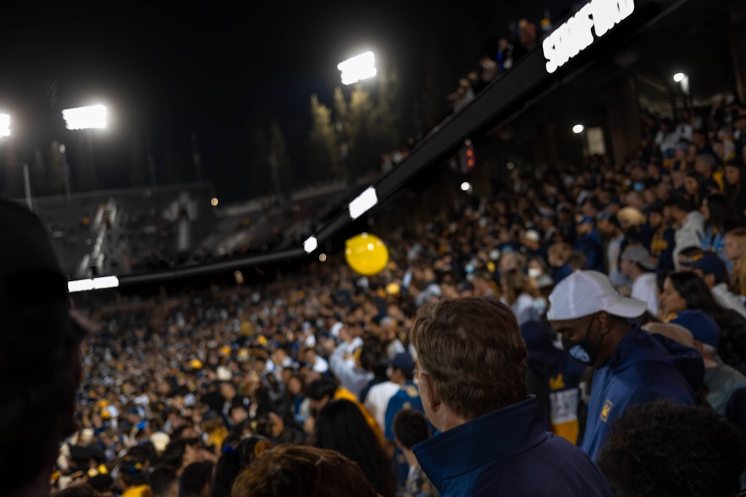 a group of people standing in front of a crowd boise stadium, blue turf, fans cheering
