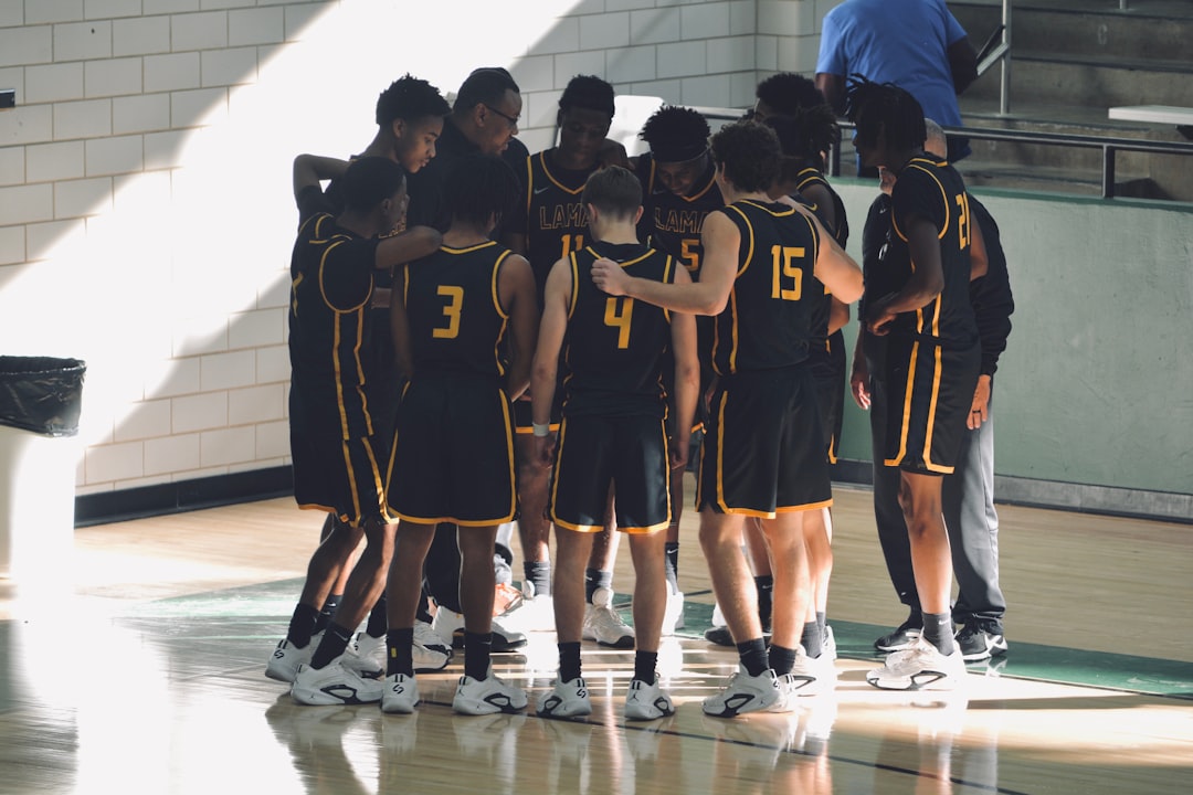 A group of young men standing on top of a basketball court teens celebrating, high school basketball court, teammates hugging, fans cheering