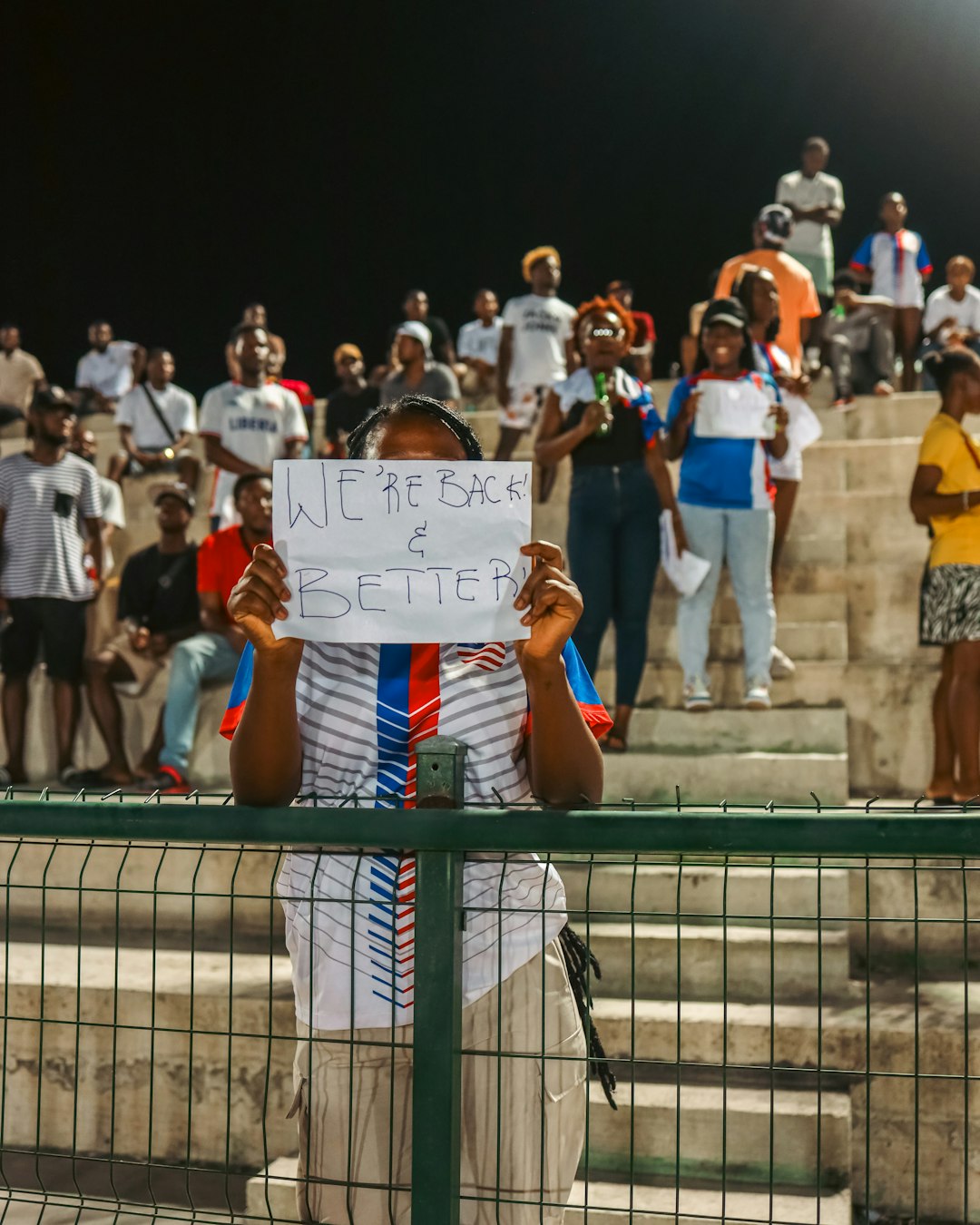 A man holding a sign in front of a crowd of people fans holding signs, stadium engagement, crowd energy