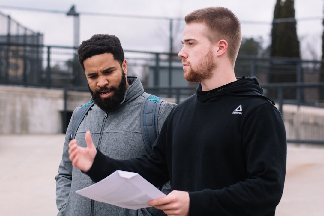 man in black hoodie holding white printer paper and man in grey zip up jacket during daytime college sports, ai recruiting, data analysis