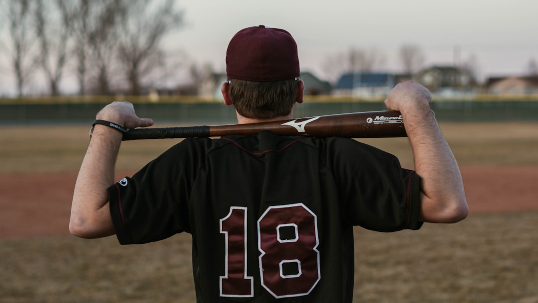 man in red and white baseball cap and black and white jersey shirt high school sports AI data