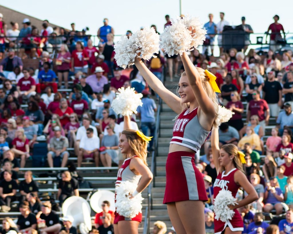 women in white and red uniform dancing on stage during daytime millikin fans, college football mascots, cheerleaders, tailgate