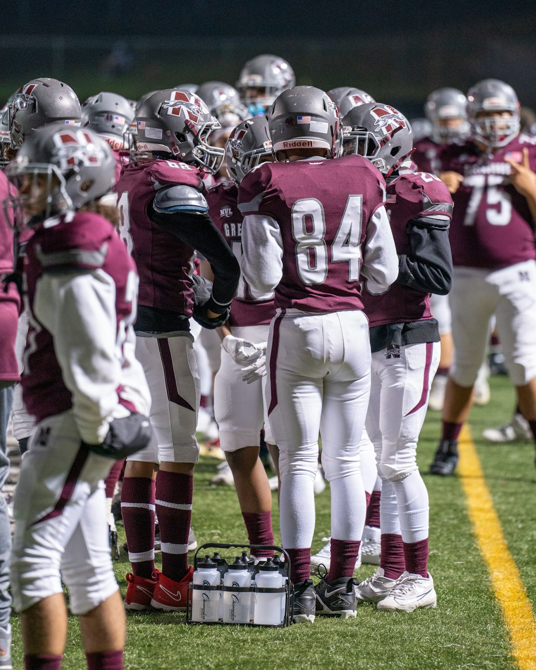 A group of football players standing on top of a field youth football, division jerseys, team huddle