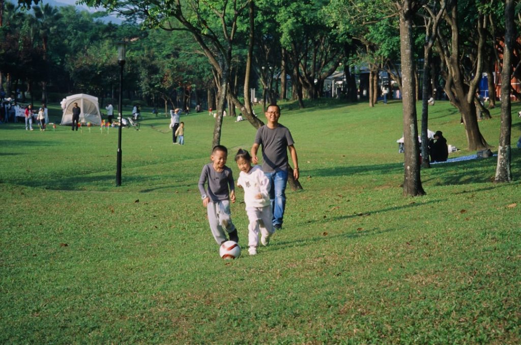 A group of people walking across a lush green park children playing, kids club, outdoor games, family vacation