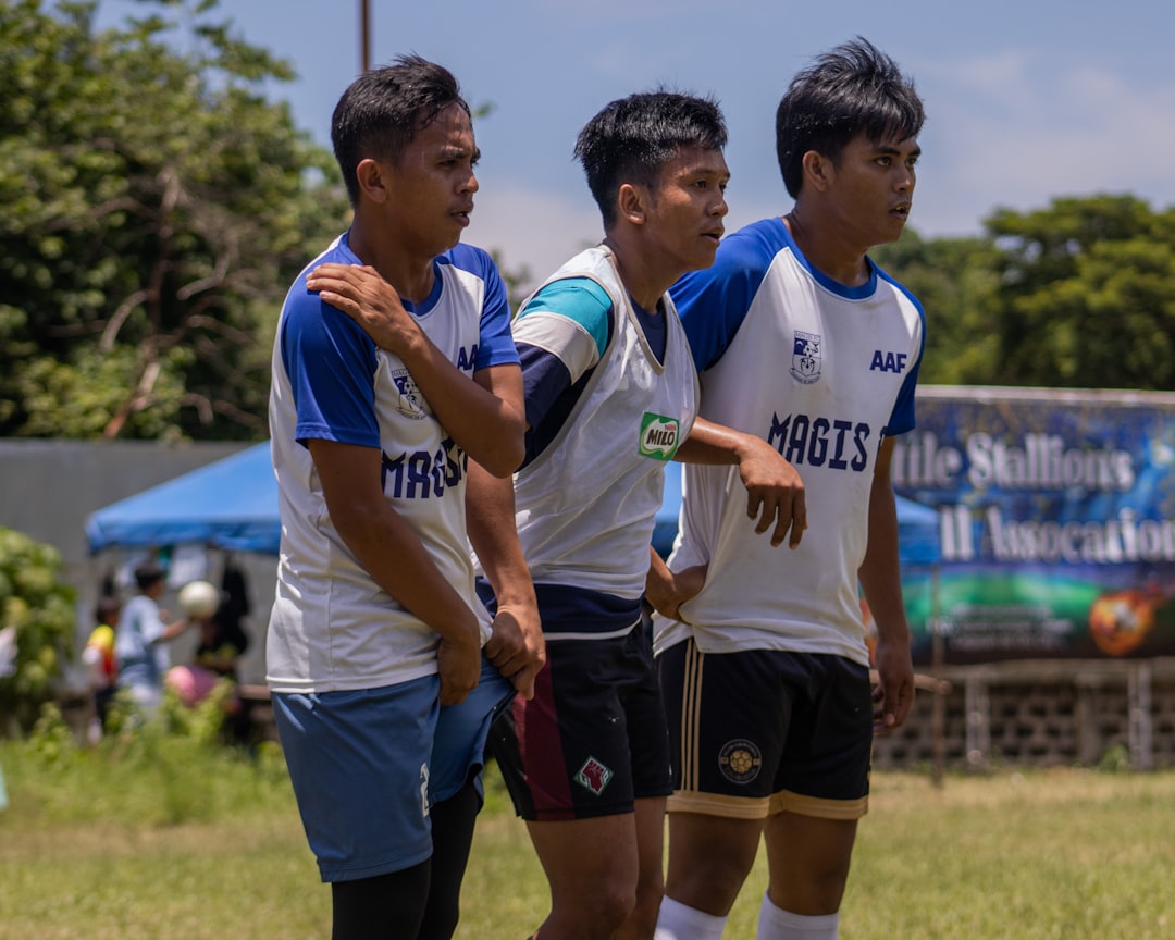 a group of young men standing next to each other on a field youth football, division jerseys, team huddle