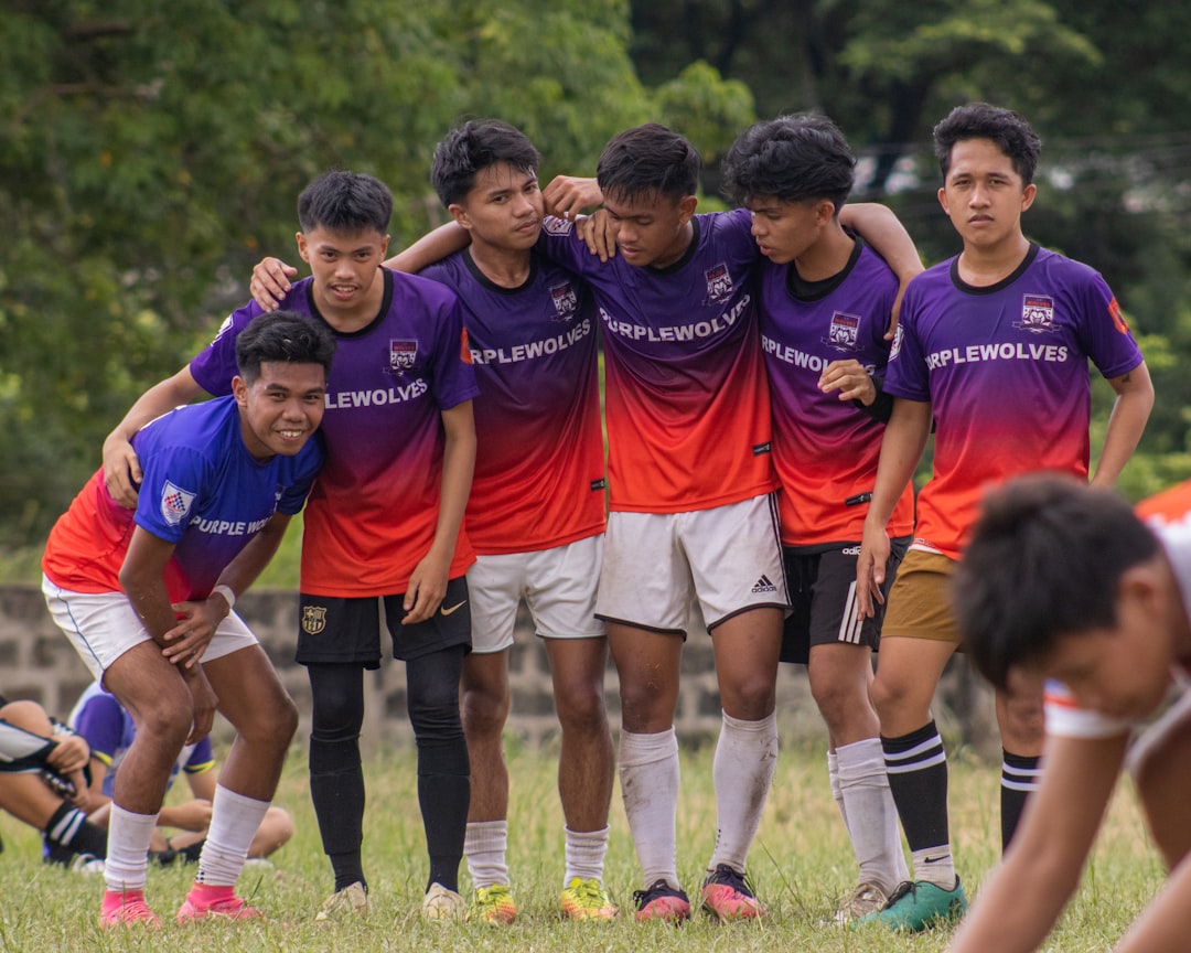 a group of young men standing next to each other on a field youth football, division jerseys, team huddle