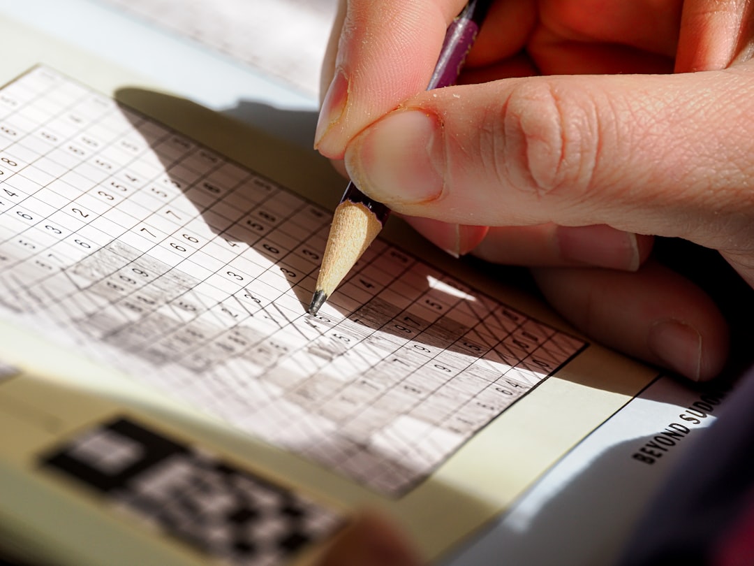 A person writing on a piece of paper with a pencil betting notebook, tracking results, sports betting record