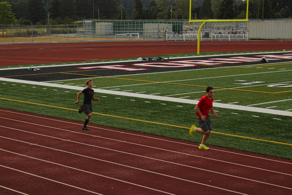 Two men running on a track in a stadium wicksburg football training, high school athletes lifting, early morning practice