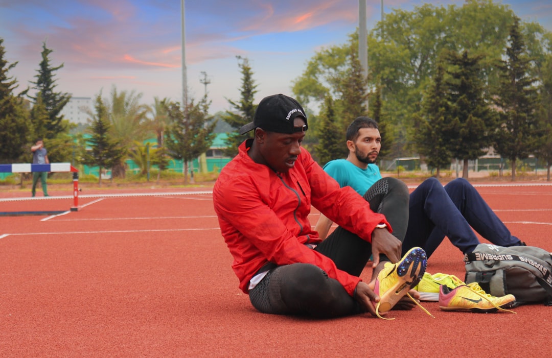 man in orange jacket and black pants sitting on ground during daytime coach athlete training session, gym consultation, athlete evaluation