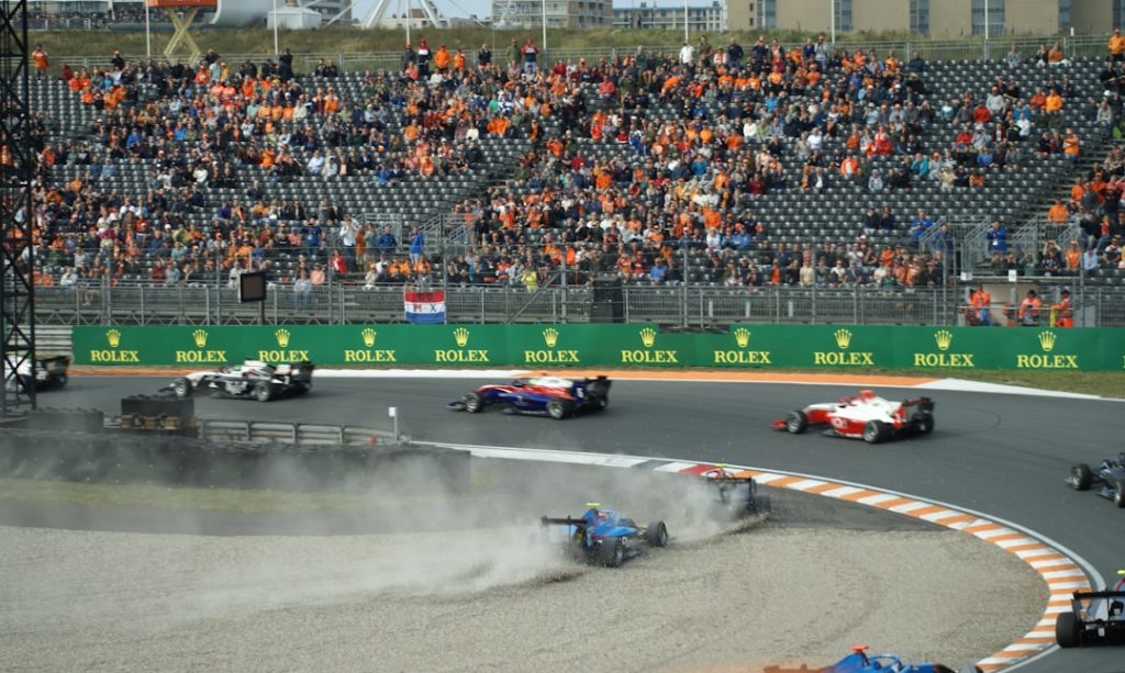 a group of race cars on a track with a crowd watching indycar oval speed race, formula 1 grand prix track