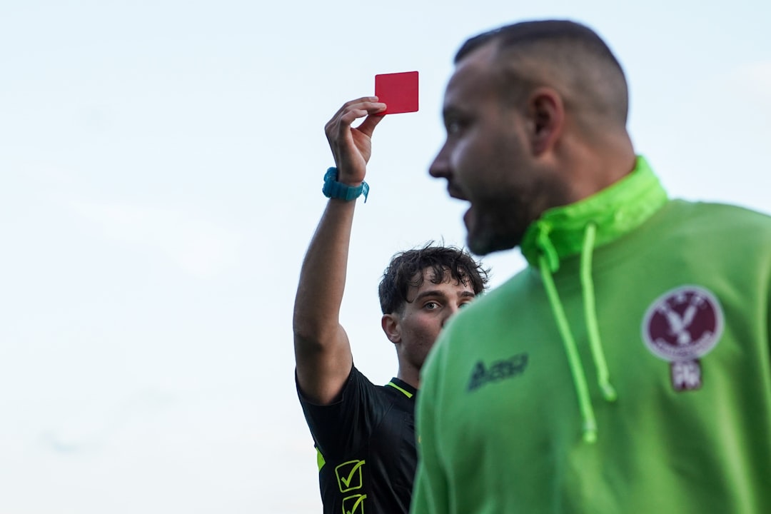 A man in a green hoodie holding up a red card football red card referee match foul