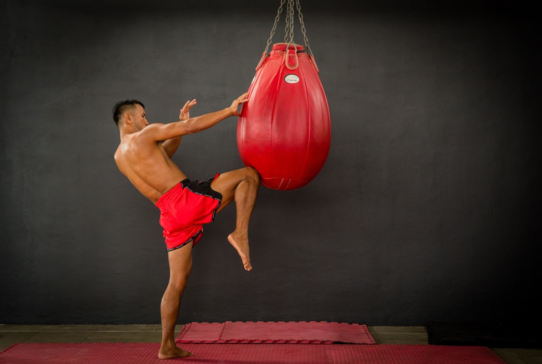 A man in red shorts kicking a red boxing bag muay thai fighters, traditional training, thailand gym