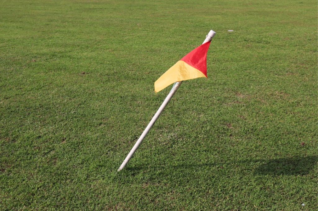 A small red and yellow flag sticking out of the grass football referee flag field blue