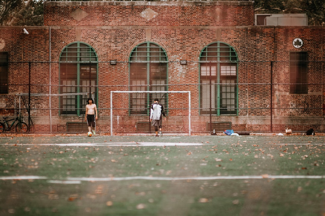 man in black jacket walking on sidewalk during daytime youth lacrosse, practice session, soft balls