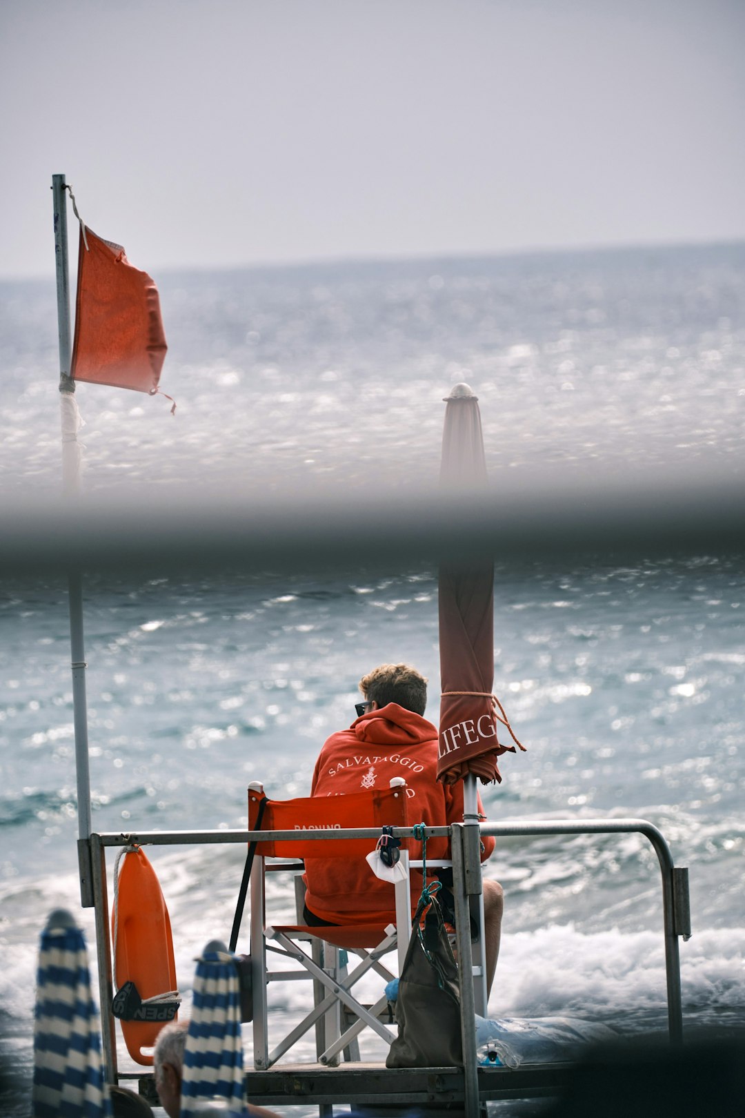 man in orange shirt holding white and red flag on beach during daytime water ski group safety boat communication signals