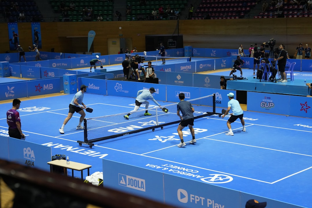 Players compete in a pickleball match on a blue court. teamwork volleyball positions indoor court