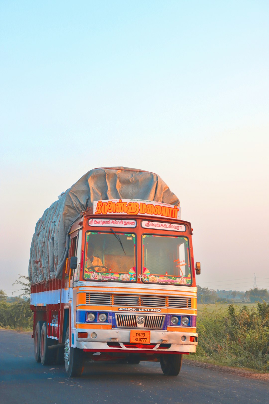 a colorful truck driving down a rural road indian roads, factory logistics, transportation issues