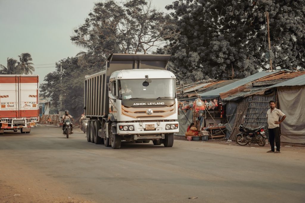 A truck driving down a street next to tents indian roads, factory logistics, transportation issues