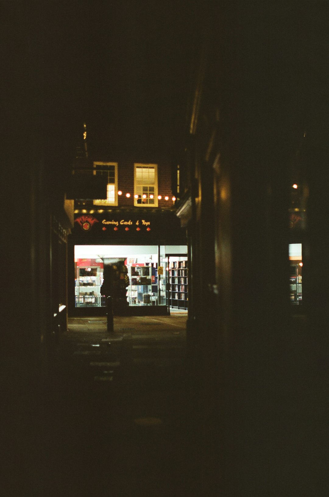 A dimly lit street with a glowing shop at night. convenience store exterior, lottery sign, storefront night lights
