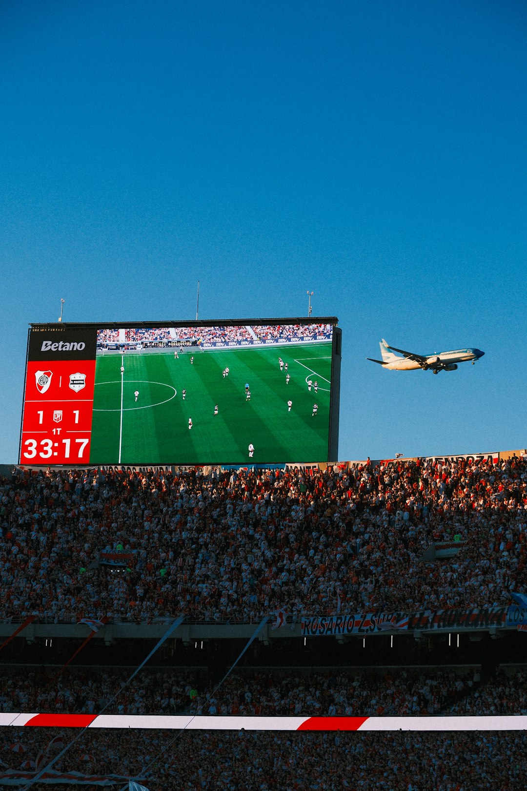 Airplane flies past stadium screen during soccer game. football party invitation on phone screen, modern sports graphics, bold typography
