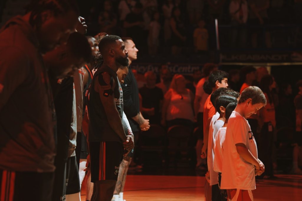 Basketball players and kids stand on the court. NBA court wide shot, tall players under basket, height comparison