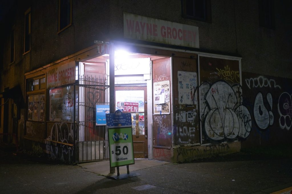 Corner grocery store at night with graffiti on wall. convenience store exterior, lottery sign, storefront night lights