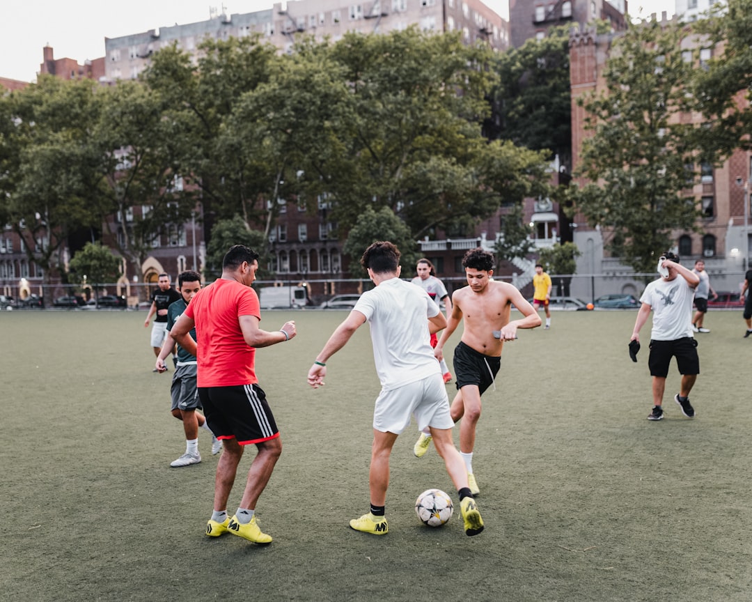 group of people playing soccer on green grass field during daytime midfield battle soccer match, players competing for ball, intense football action