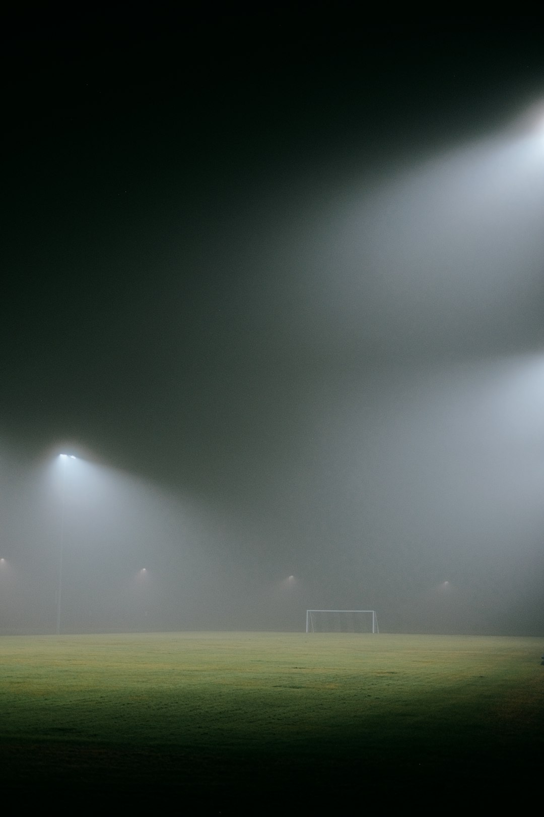 A foggy soccer field with three lights football field goal attempt, stadium lights night game, football sailing wide