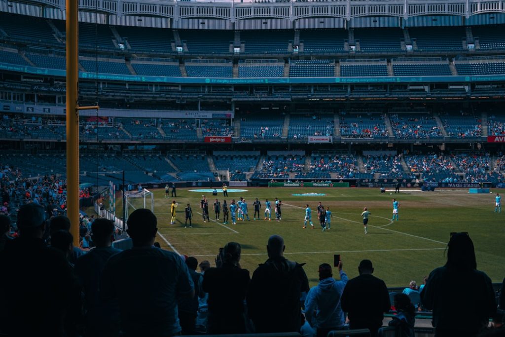 a group of people standing on top of a soccer field football third down play, nfl coaches sideline discussion, packed stadium crowd cheering