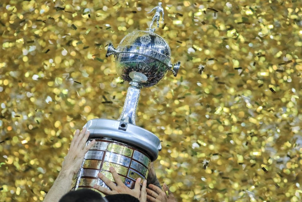 A person holding a trophy in front of a wall of confetti concacaf champions league trophy close up, captain lifting trophy, confetti celebration soccer, championship podium