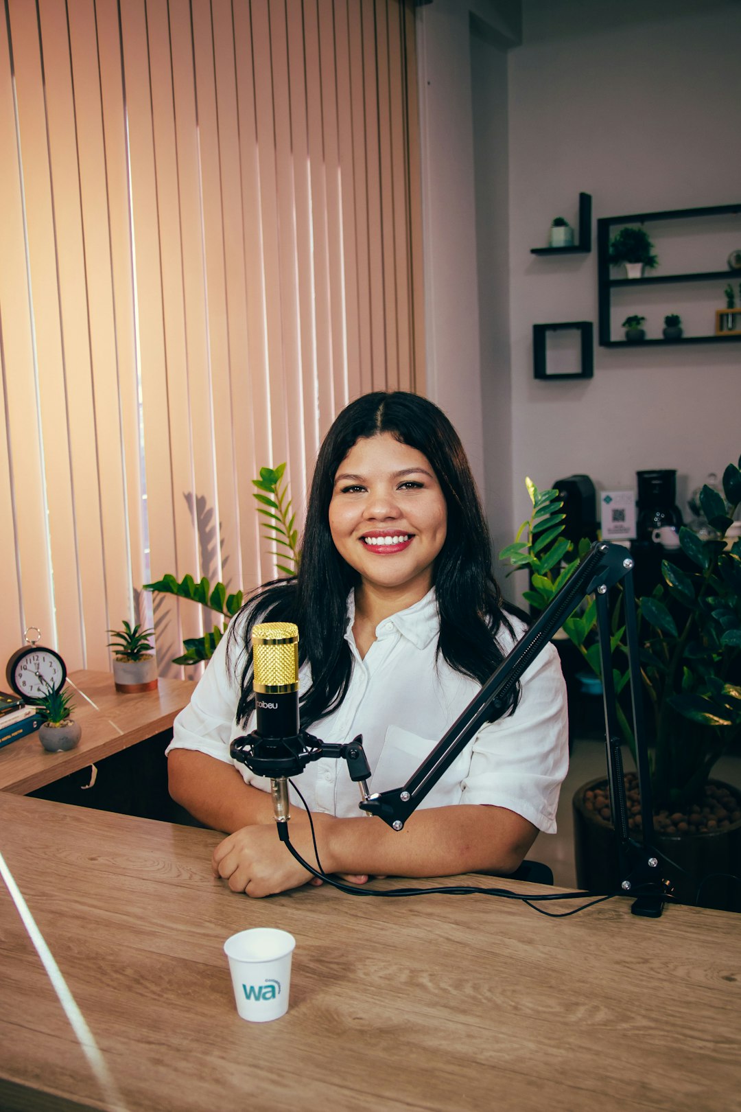 a woman sitting at a desk with a microphone podcast studio microphones, women hosting podcast, colorful recording setup