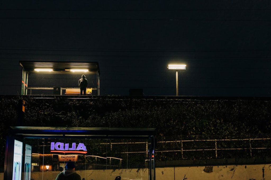 man standing under waiting shed football stadium night game crowd, nfl field action, scoreboard lights