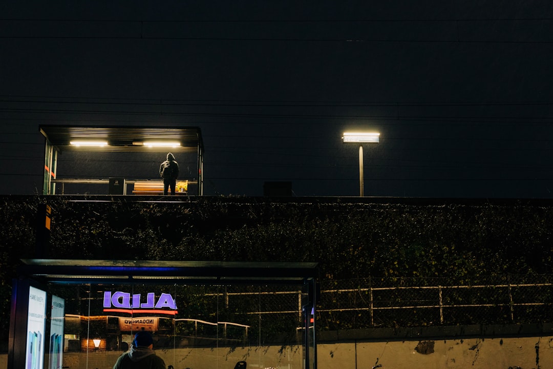 man standing under waiting shed football stadium night game crowd, nfl field action, scoreboard lights