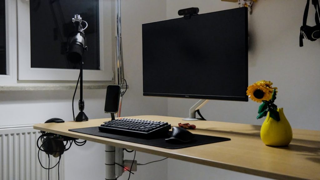 A computer desk with monitor, keyboard, and sunflower. music artist typing bio, home studio setup, creative workspace