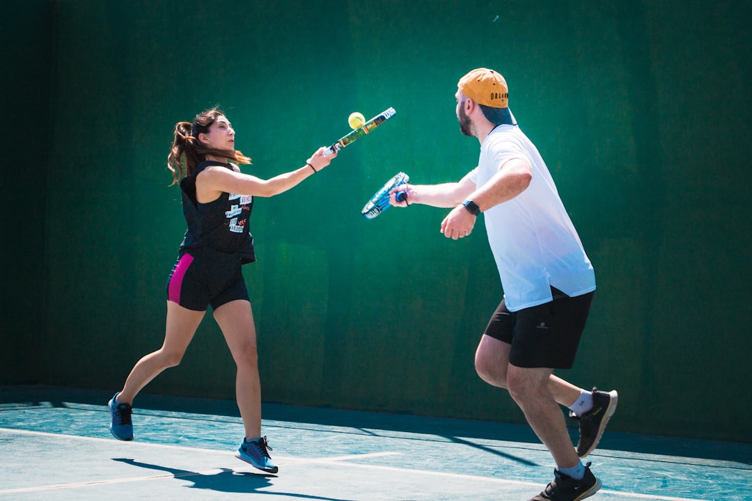 a man and a woman playing tennis on a tennis court padel smash angle shot glass wall opponent defending