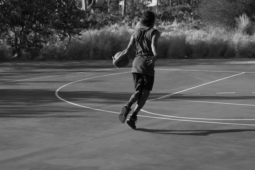 A person dribbling a basketball on an outdoor court. basketball pull up jump shot, outdoor court action, player mid air release