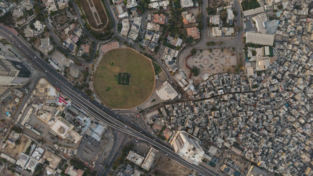 Aerial view of a city with a large oval stadium. cricket ground aerial view, cricket stadium local, cricket pitch neighborhood