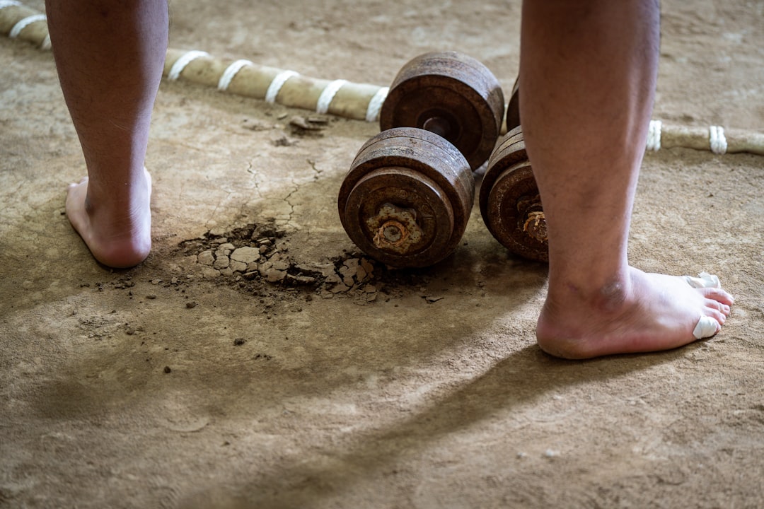 Bare feet near old weights on dirt ground athlete foam rolling leg, gym floor, recovery session