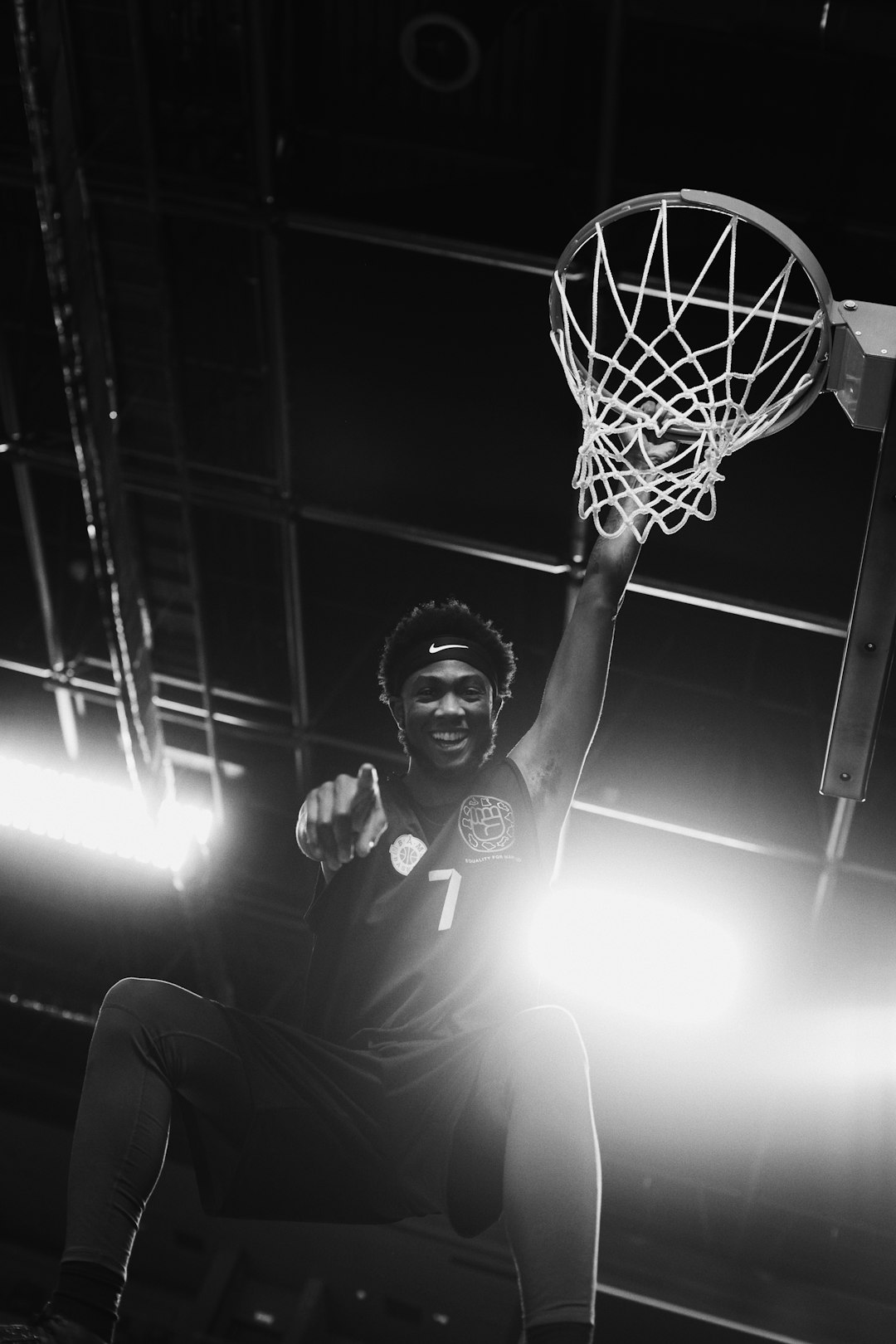 Basketball player pointing at camera near hoop basketball buzzer beater shot, indoor arena lights, dramatic jump shot