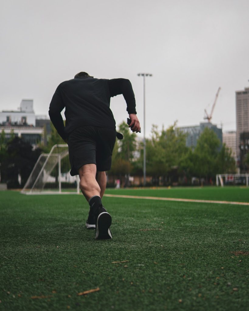 man in black long sleeve shirt and black shorts running on green grass field during daytime football player jogging training field cones