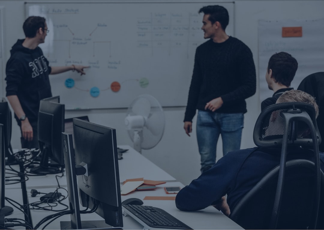man in black sweater and blue denim jeans sitting on black chair team developers discussing api design whiteboard laptops
