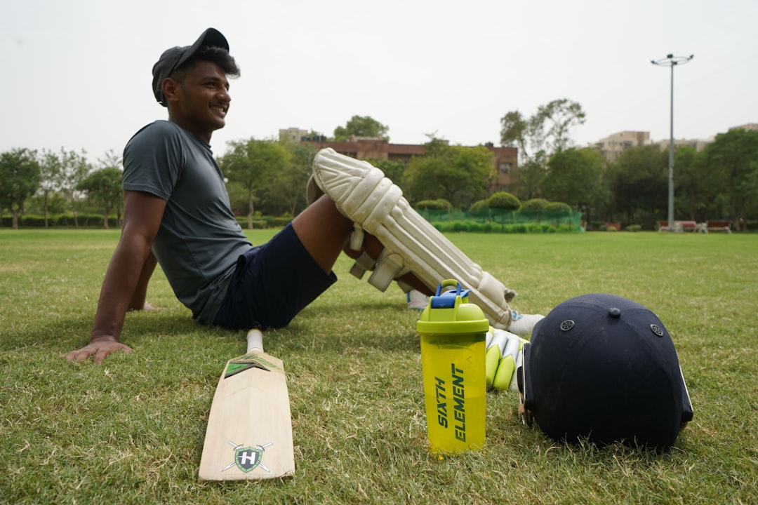 man in gray t shirt and black cap holding white plastic bottle cricket warm up, dynamic stretching, amateur players field